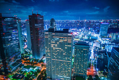 Illuminated modern buildings in city against sky at night