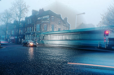 Cars on road by buildings in city during rainy season