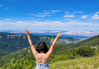 Woman on top of hill with arms raised, view, sea, summer, travel, vacation.