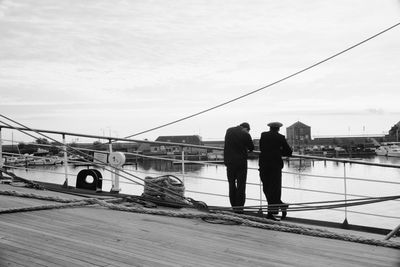 Rear view of men standing on bridge against sky