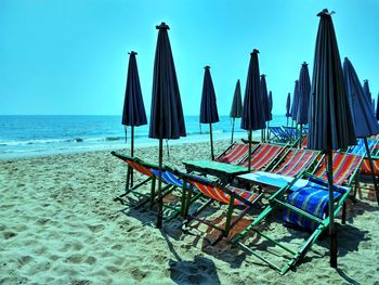 Empty chairs on beach by sea against sky