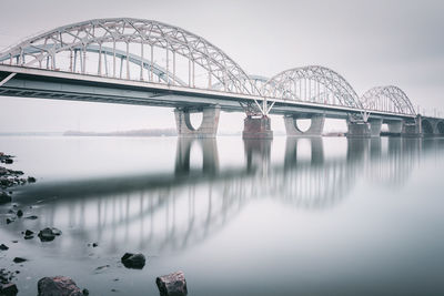 New darnytskyi bridge over dnieper river with reflection against sky