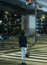 Rear view of woman standing on railroad tracks in city at night