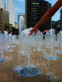 Woman hand touching water of fountain in city