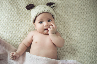 Portrait of cute baby girl in knit hat lying on bed