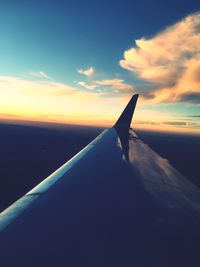 Airplane wing over sea against sky during sunset