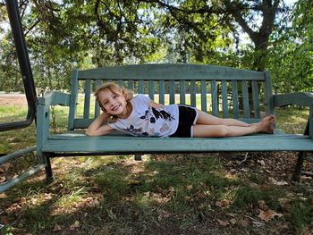 Portrait of smiling girl sitting on wood against trees