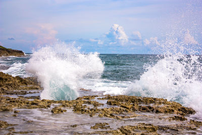 Waves splashing on rocks at shore against sky