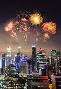 Firework display over illuminated buildings against sky at night