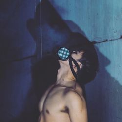 Side view of shirtless man wearing gas mask by blue wall