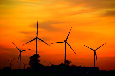 Silhouette wind turbines on field against orange sky