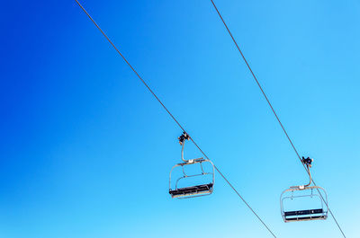 Low angle view of overhead cable cars against clear blue sky