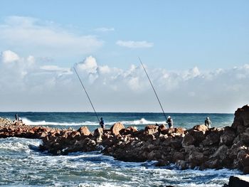 Group of people on rocks by sea against sky