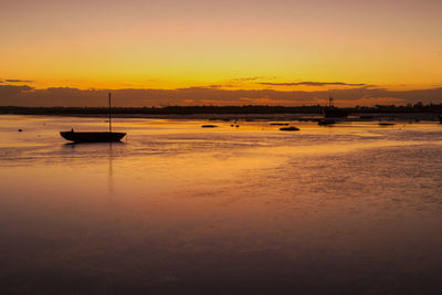 Silhouette boats moored on sea against orange sky