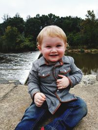 Portrait of cute boy sitting against river