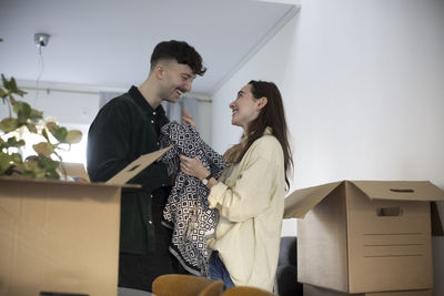 Happy young couple holding blanket while standing amidst boxes in new house