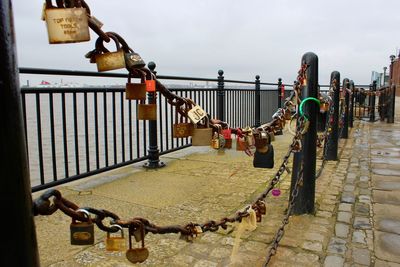 Padlocks hanging on railing by bridge against sky