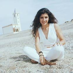 Young woman sitting on sand at beach against sky