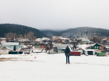 Rear view of person looking at houses and mountains against sky