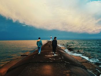 Rear view of men standing on beach against sky