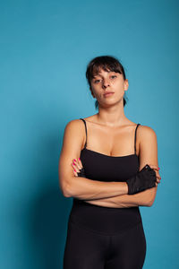 Portrait of young woman standing against blue background