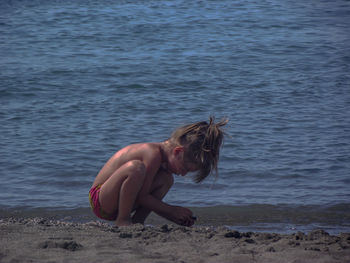 Full length of shirtless girl playing with sand at beach