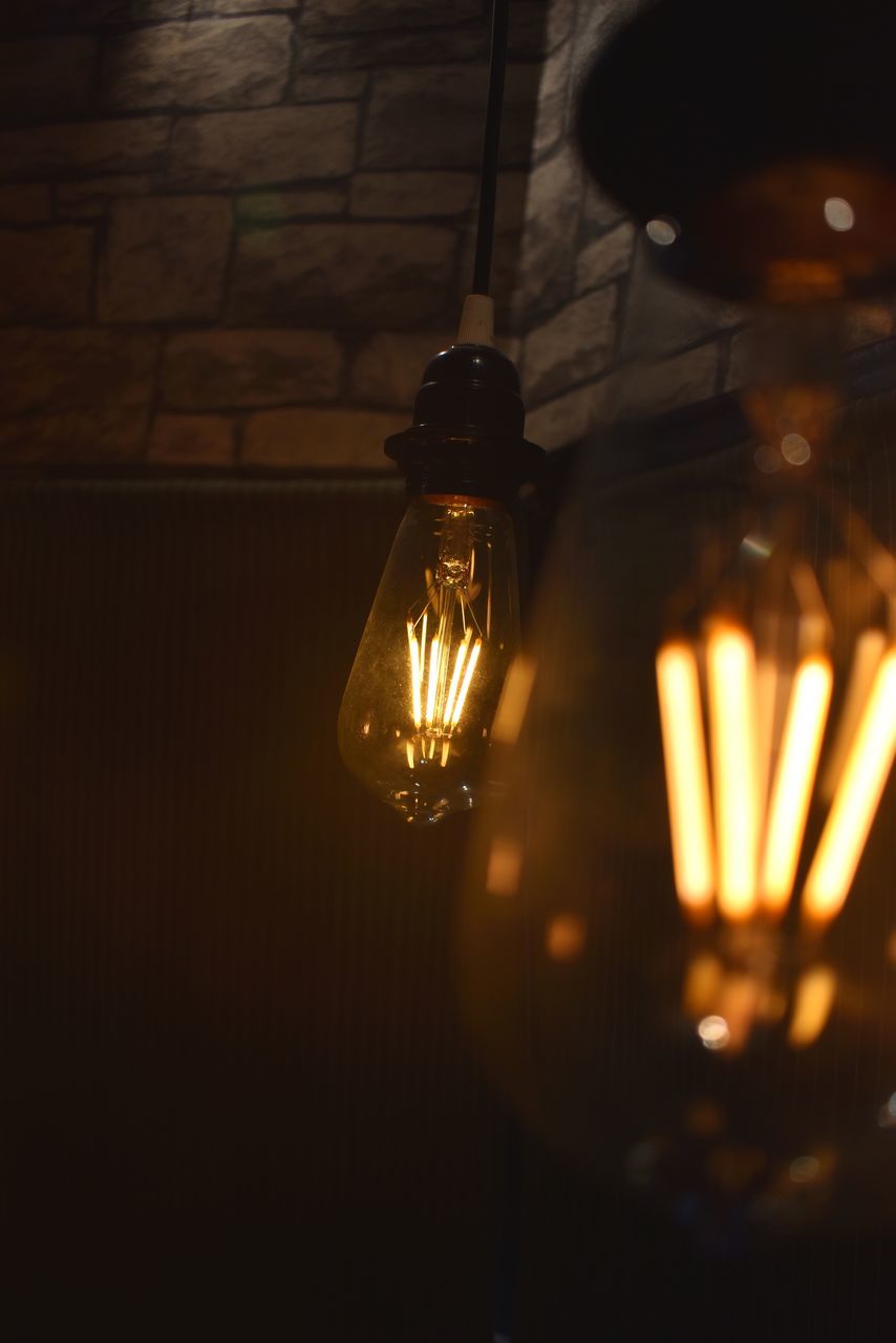 CLOSE-UP OF ILLUMINATED LIGHT BULB HANGING FROM CEILING