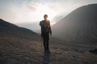 Rear view of backpack woman standing on land by mountains