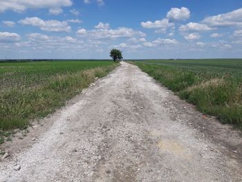 Dirt road amidst field against sky