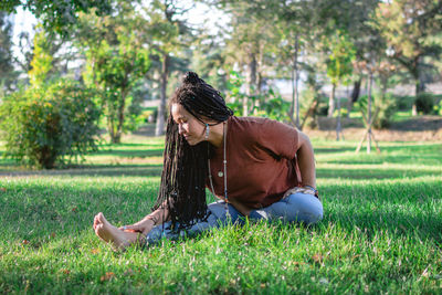 Young woman with long african braids is doing yoga outside in a park. concept of healthy lifestyle.