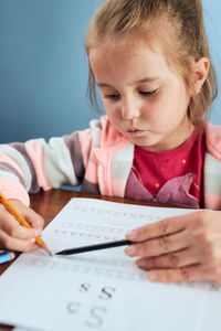 Little girl preschooler learning to write letters with help of her tutor
