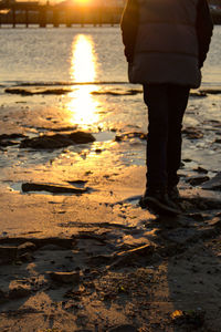 Low section of woman standing on beach at sunset