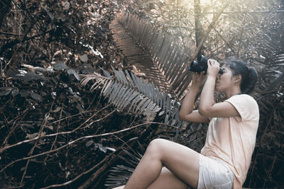 Young woman looking thorough binoculars in forest