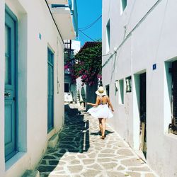 Rear view of woman walking on alley amidst buildings during sunny day