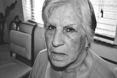 Close-up portrait of senior woman by window at home