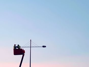 Low angle view of men in cherry picker repairing light against clear sky