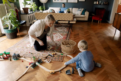 Mother looking at daughter playing with train set in living room