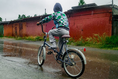 Boy riding bicycle on road during rainy season