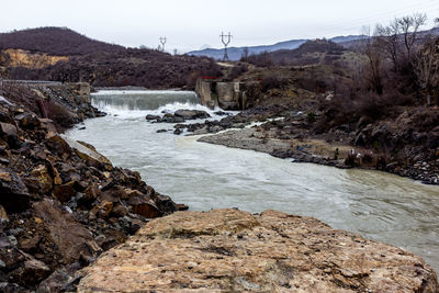 Scenic view of river flowing by mountains against sky