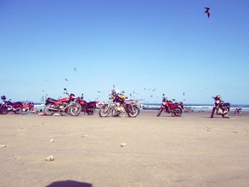 People riding bicycle on sand against clear sky