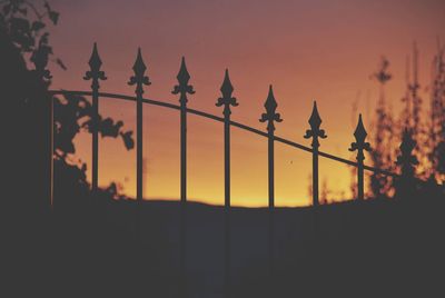 Silhouette fence against orange sky during sunset