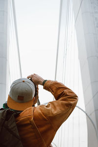 Rear view of man photographing bridge against sky