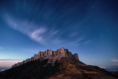 Twilight panoramic mountain view, starry sky and clouds, city lights in the background