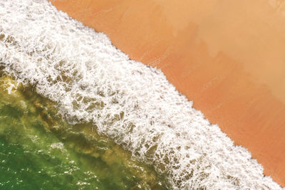 Aerial image of white surf splashing on a sandy beach with emerald green ocean
