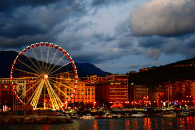 Illuminated ferris wheel in city against sky at night