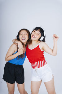 Lesbian couple listening music while dancing against gray background