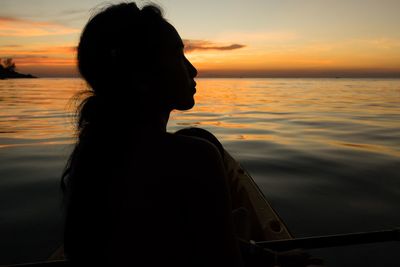 Silhouette woman sitting on kayak in sea against sky during sunset