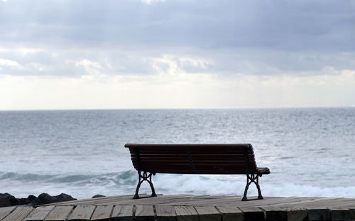 Empty bench by sea against sky