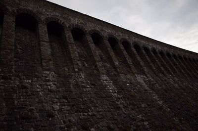 Low angle view of brick wall against cloudy sky