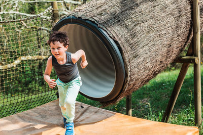 Happy active little boy running after riding tube slide on sunny summer day in adventure park